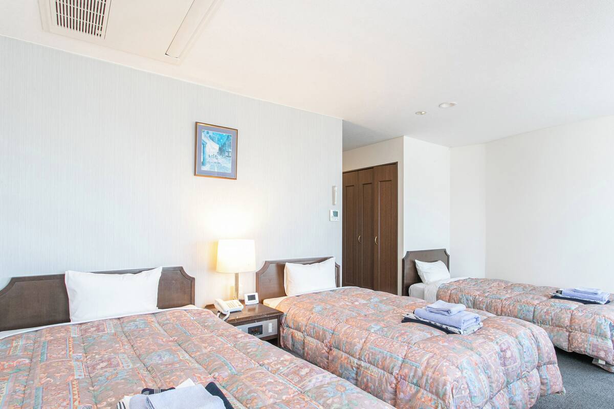 A hotel room with two beds, a nightstand with a lamp, a phone, and a door leading to another room.