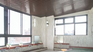 A swimming pool area with tiled walls, large windows, and a wooden ceiling. - Aqua Garden Hotel Fukumaru (Kagoshima)