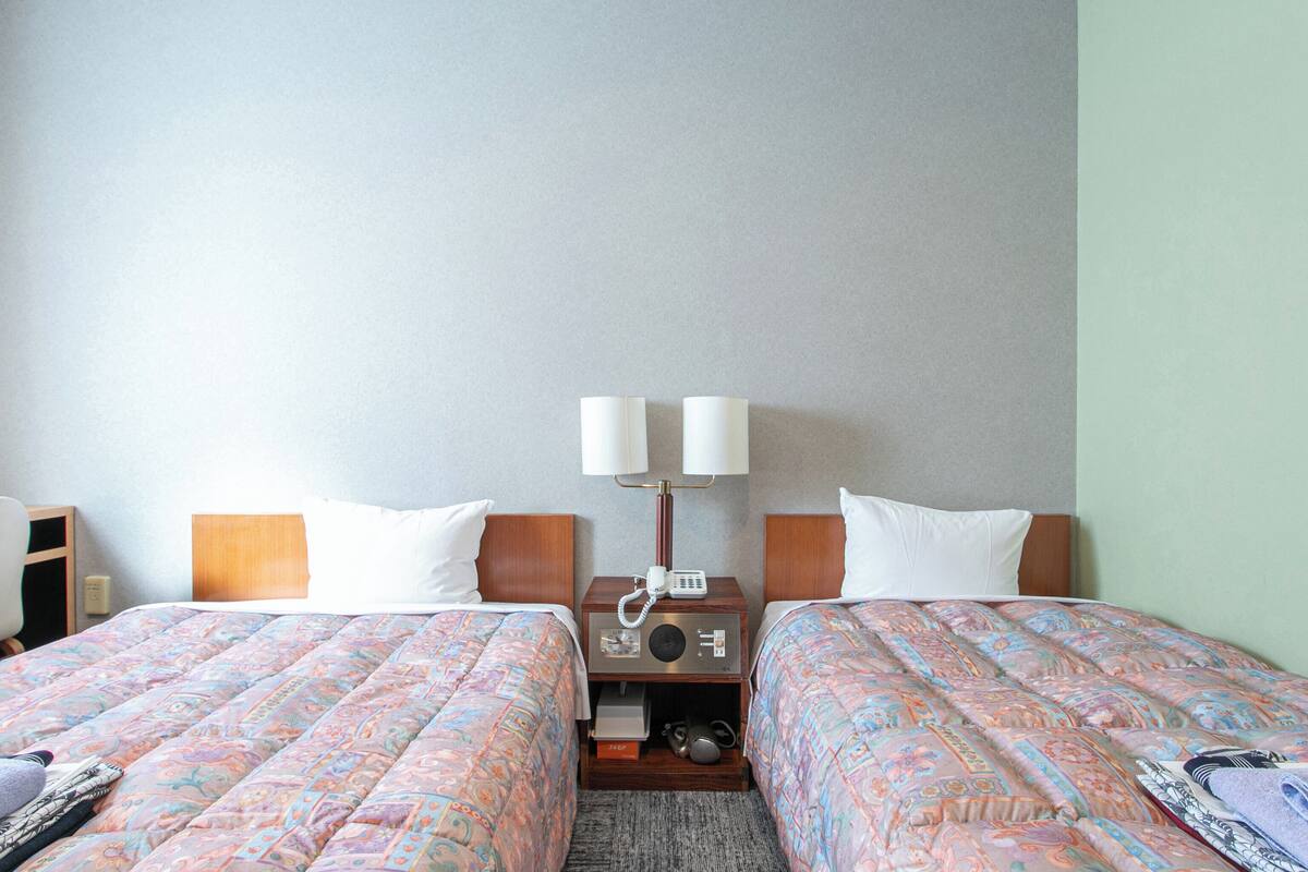 A hotel room with two beds, a nightstand with a lamp, a radio, and a small table.