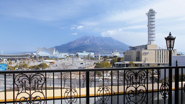 A coastal cityscape with a prominent mountain in the background, modern buildings, and a tall structure with antennas. - Aqua Garden Hotel Fukumaru (Kagoshima)