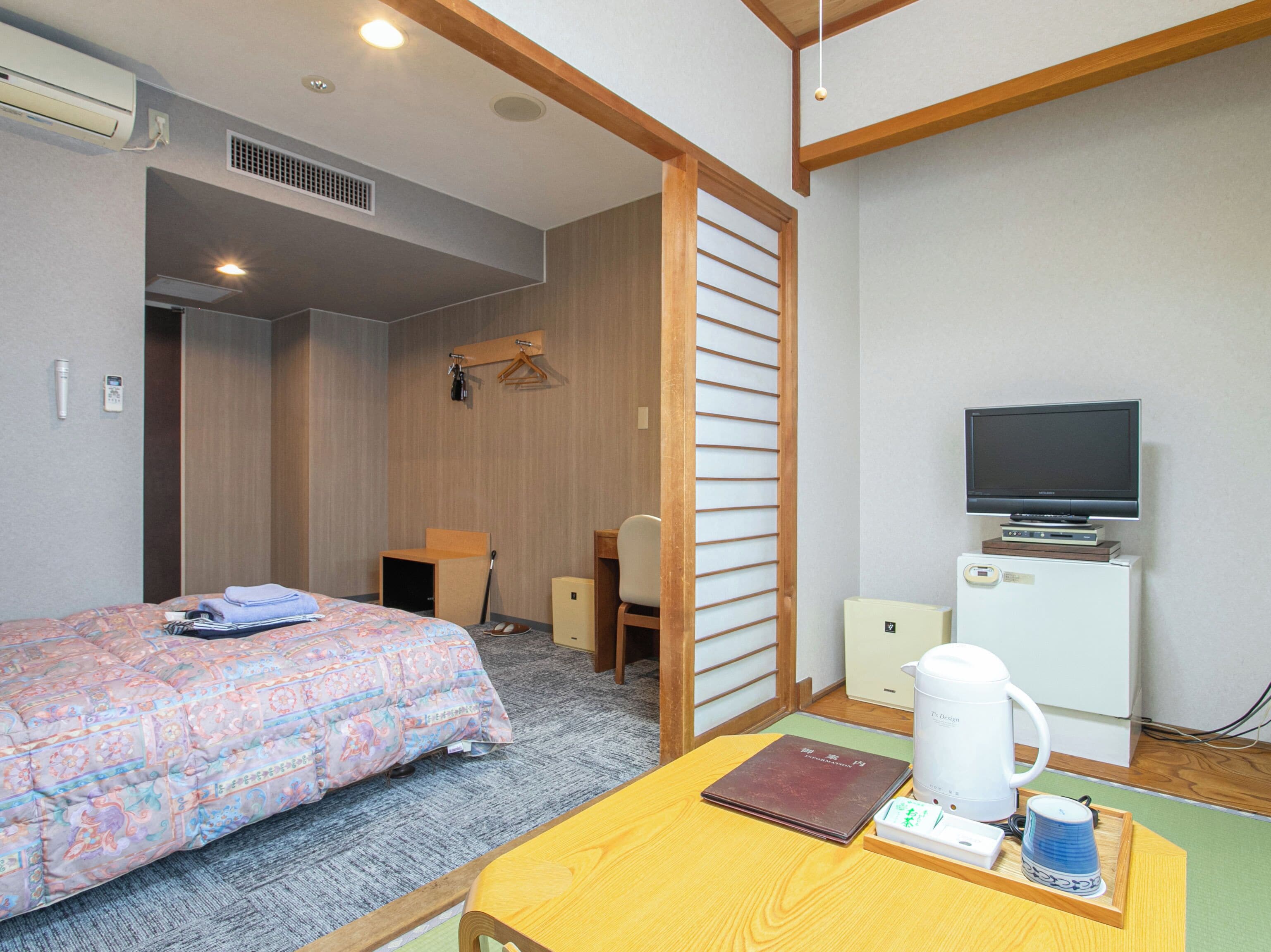 A hotel room with a bed, a desk, a television, a coffee maker, and a wardrobe.