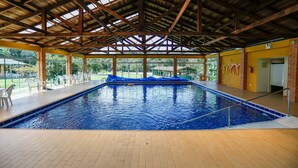 An indoor swimming pool with a wooden ceiling, tiled floor, and a view of a green outdoor area. - Palmas Hotel & Spa (Governador Celso Ramos)