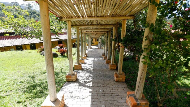 A covered walkway with wooden pillars and brick flooring, leading to a building with a tiled roof. - Palmas Hotel & Spa (Governador Celso Ramos)