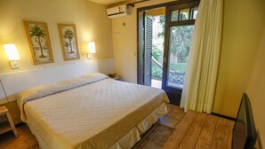 A hotel room with a large bed, a wooden floor, a television, and a balcony with curtains. - Palmas Hotel & Spa (Governador Celso Ramos)