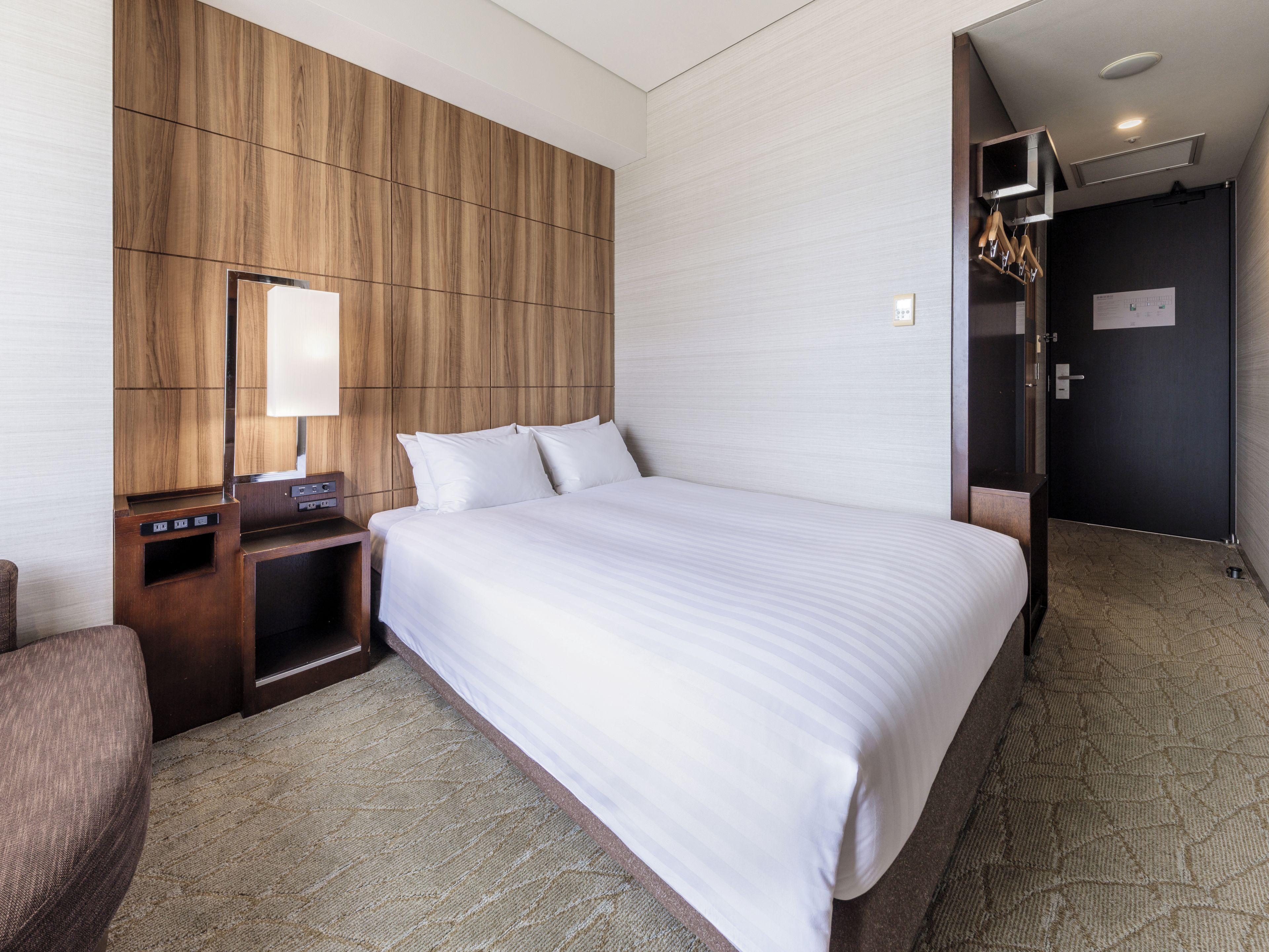 A hotel room with a large bed, a wooden panel wall, a flat-screen TV, and a small desk with a lamp.