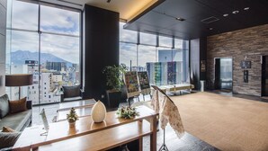 A modern hotel lobby with large windows, a reception desk, seating area, and an elevator.