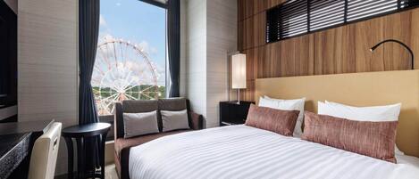 A hotel room with a large bed, a desk, a chair, a nightstand, and a lamp. There is a window with a view of a Ferris wheel.