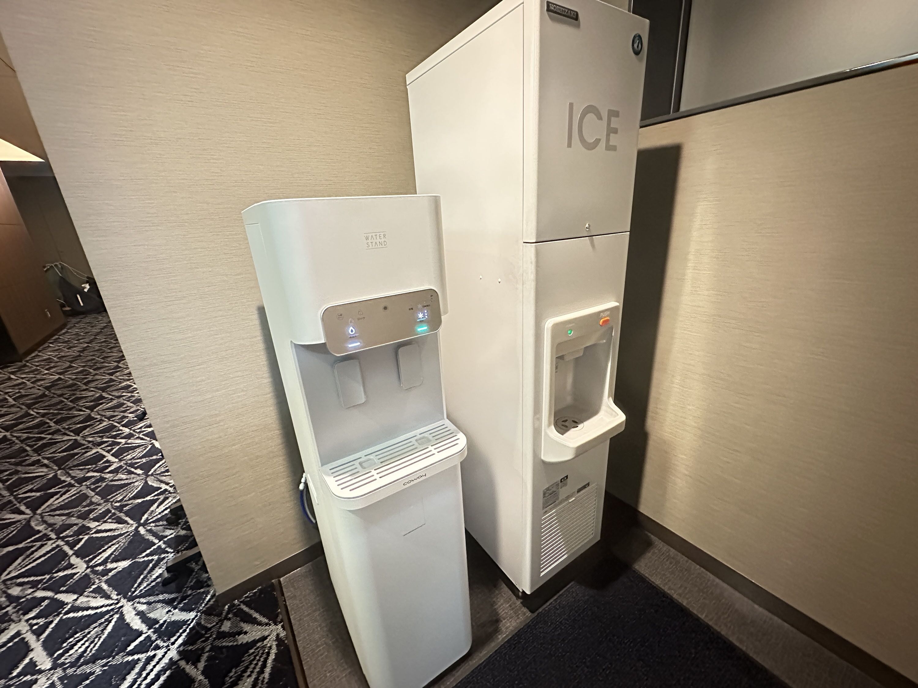 A water dispenser and a refrigerator in a hotel hallway.