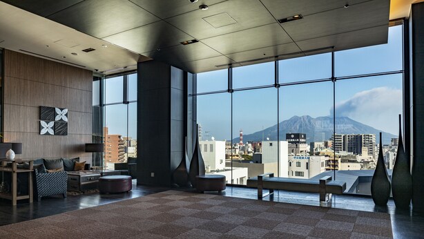 A spacious room with a large window offering a city view and a mountain in the distance.
