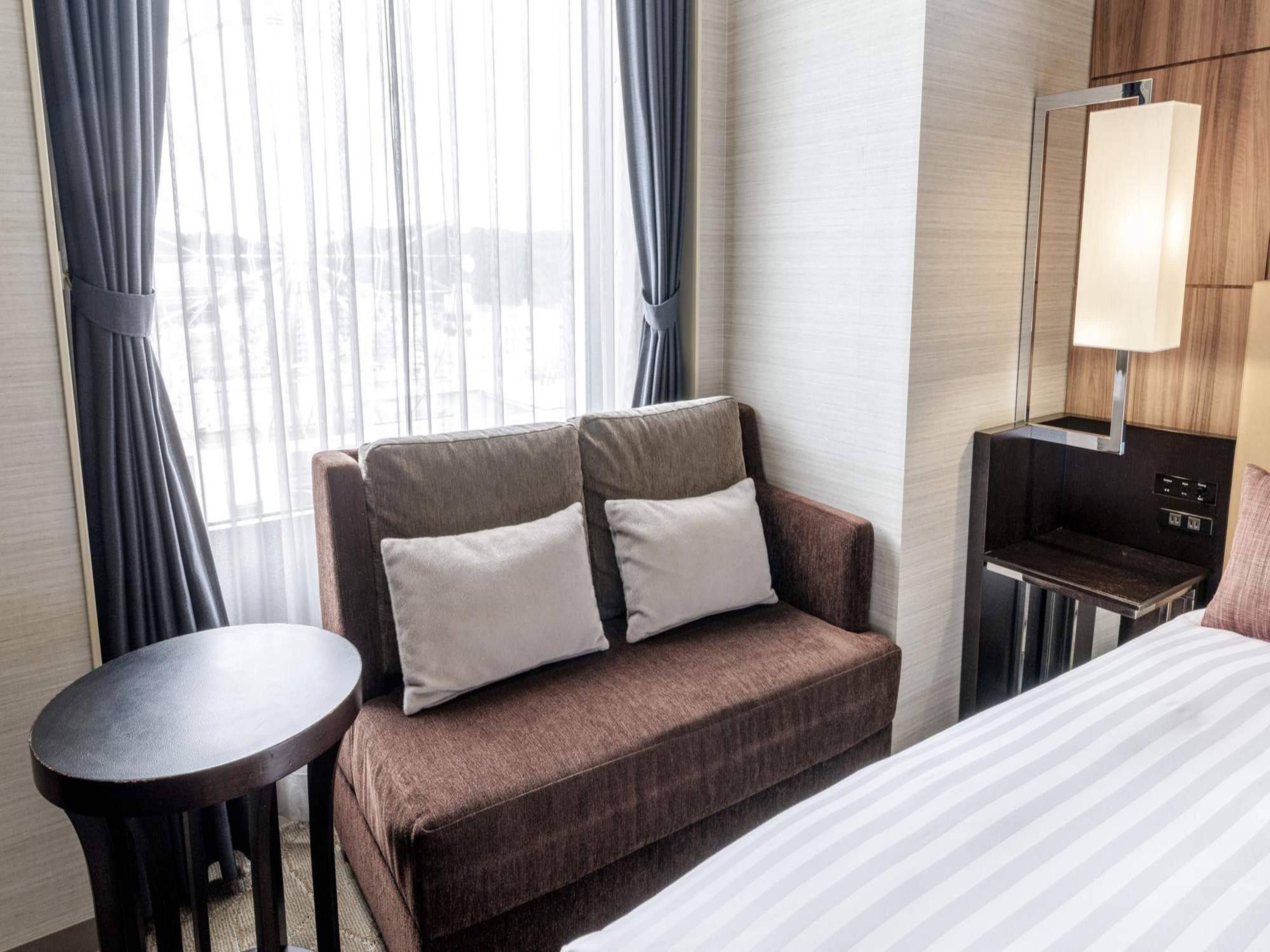 A hotel room with a sofa, a small table, a bed, and a desk with a lamp.