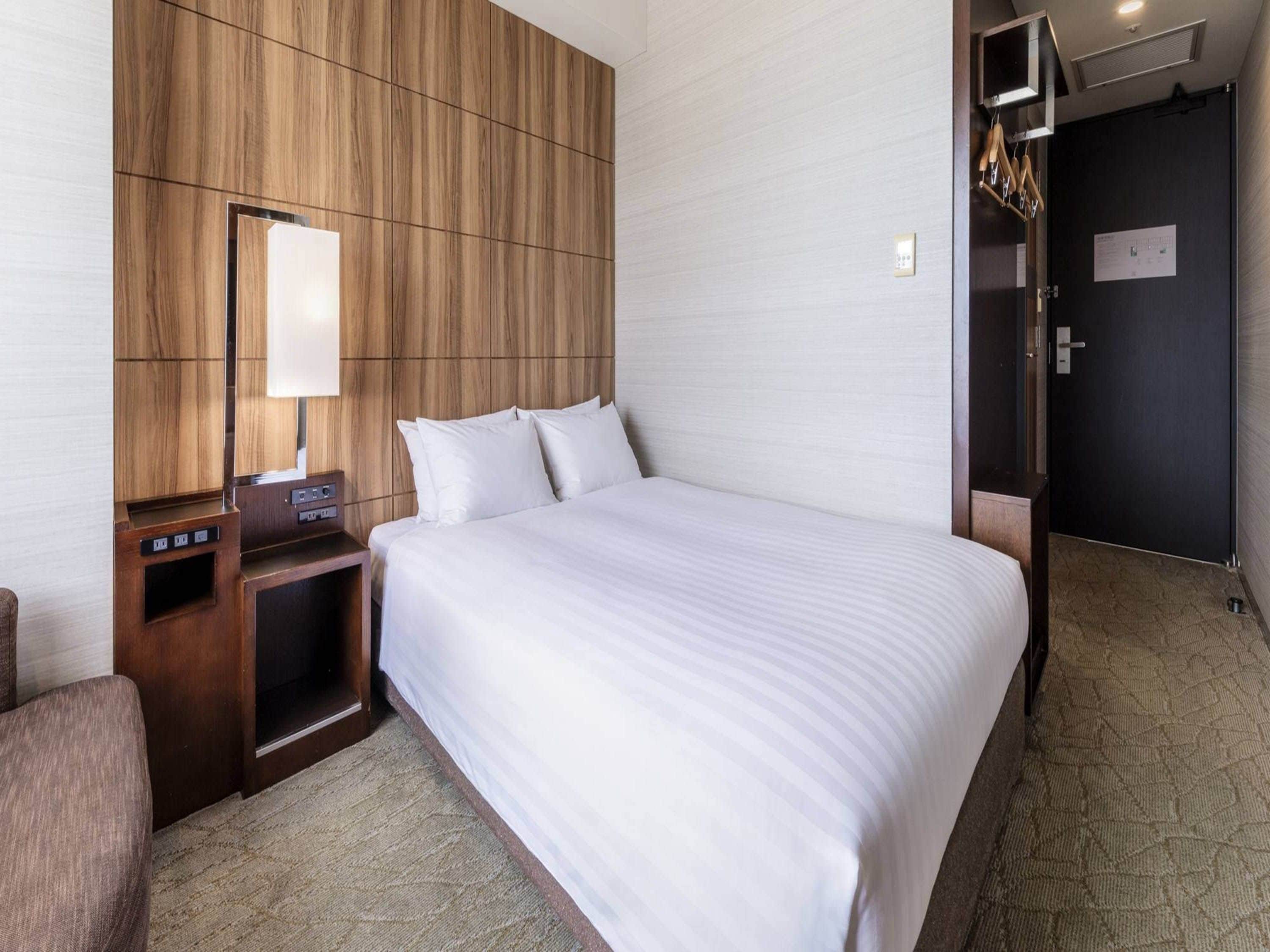 A hotel room with a large bed, a wooden headboard, a bedside table with a lamp, and a door with a mirror.