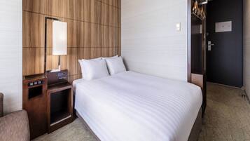 A hotel room with a large bed, a wooden headboard, a bedside table with a lamp, and a door with a mirror.