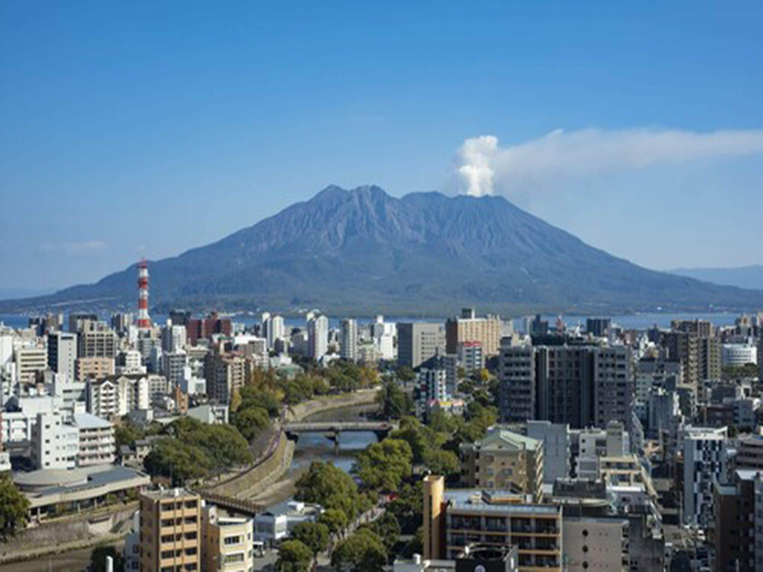 A cityscape with a prominent mountain in the background, a body of water, and a bridge connecting two areas.