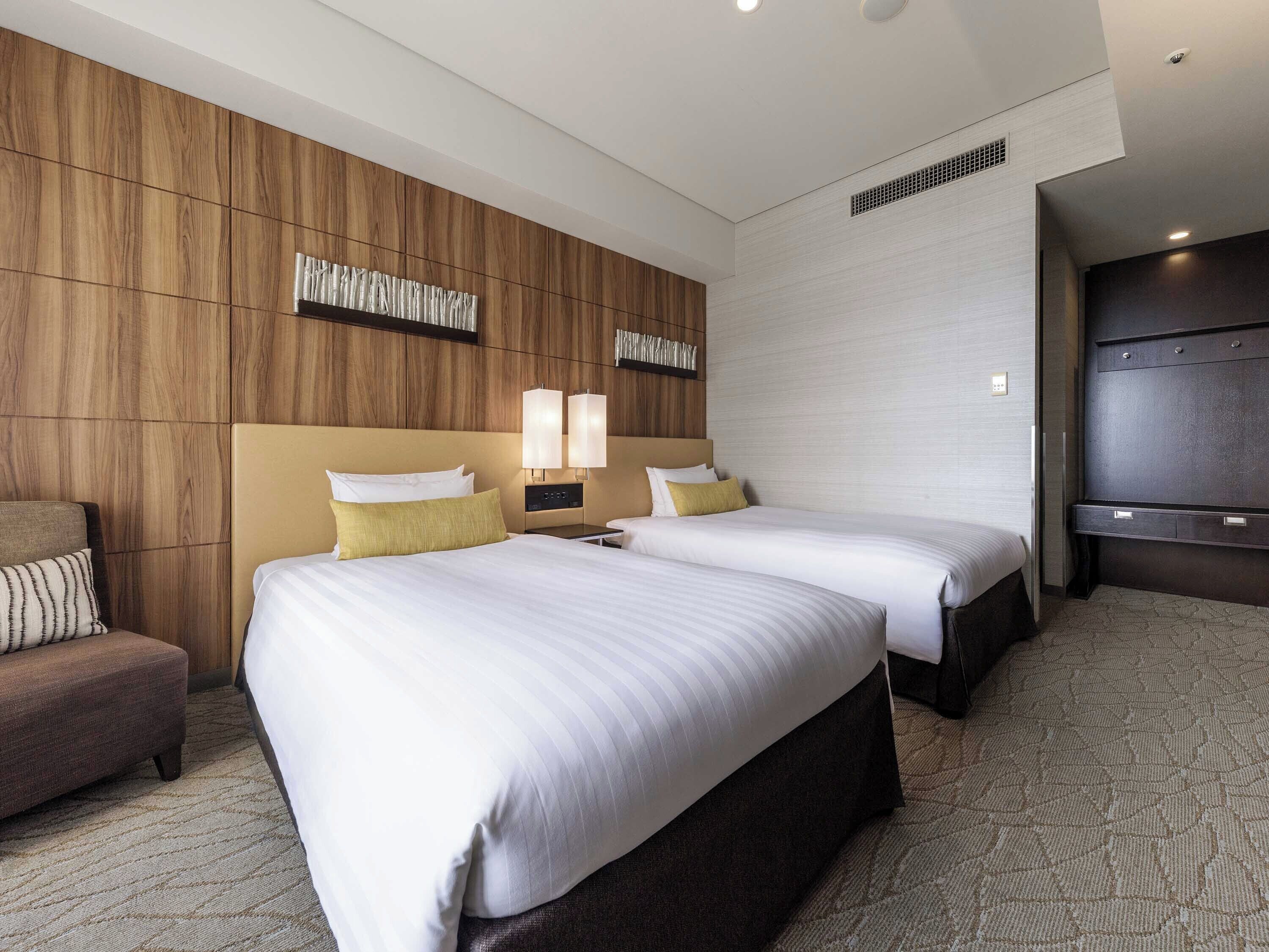 A hotel room with two beds, a sofa, a TV, and a wooden accent wall.