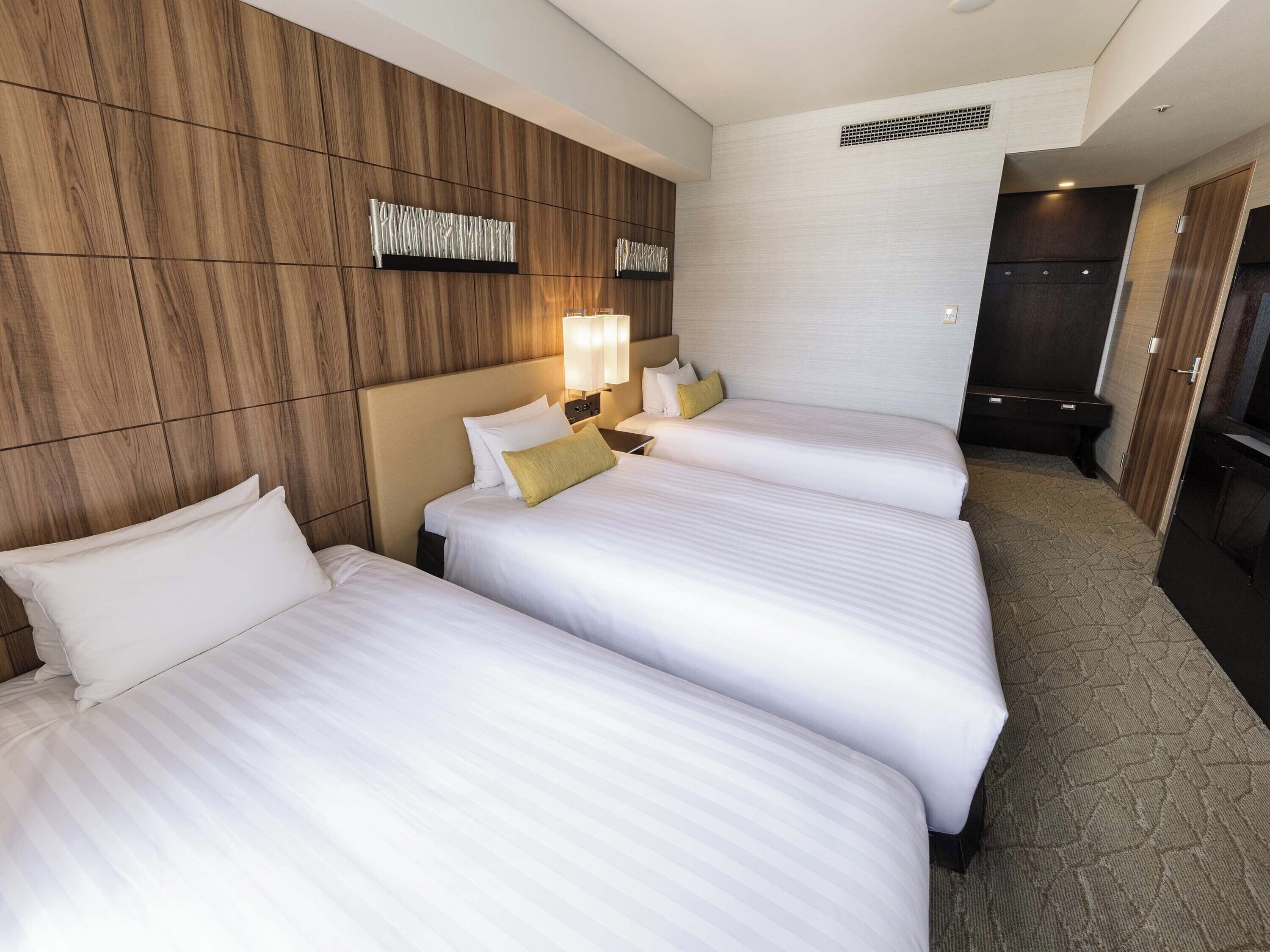 Habitación de hotel con tres camas, paneles de madera en las paredes y un espejo grande.