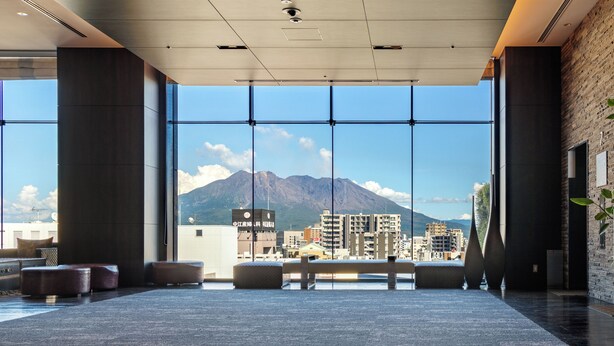 A spacious lobby with large windows offering a view of a cityscape and a mountain. - Solaria Nishitetsu Hotel Kagoshima (Kagoshima)