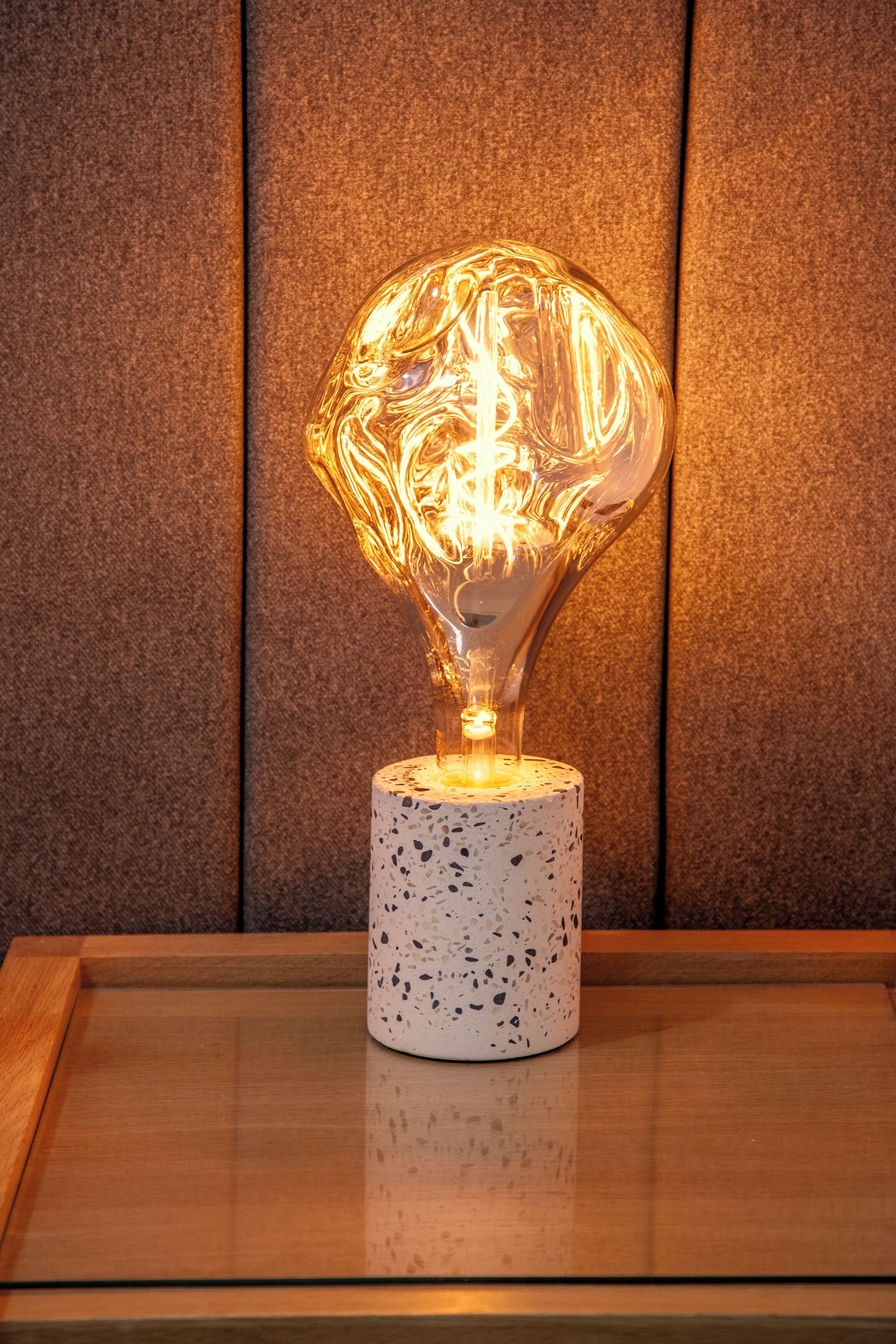 A modern light fixture with a unique glass design on a speckled pedestal base.