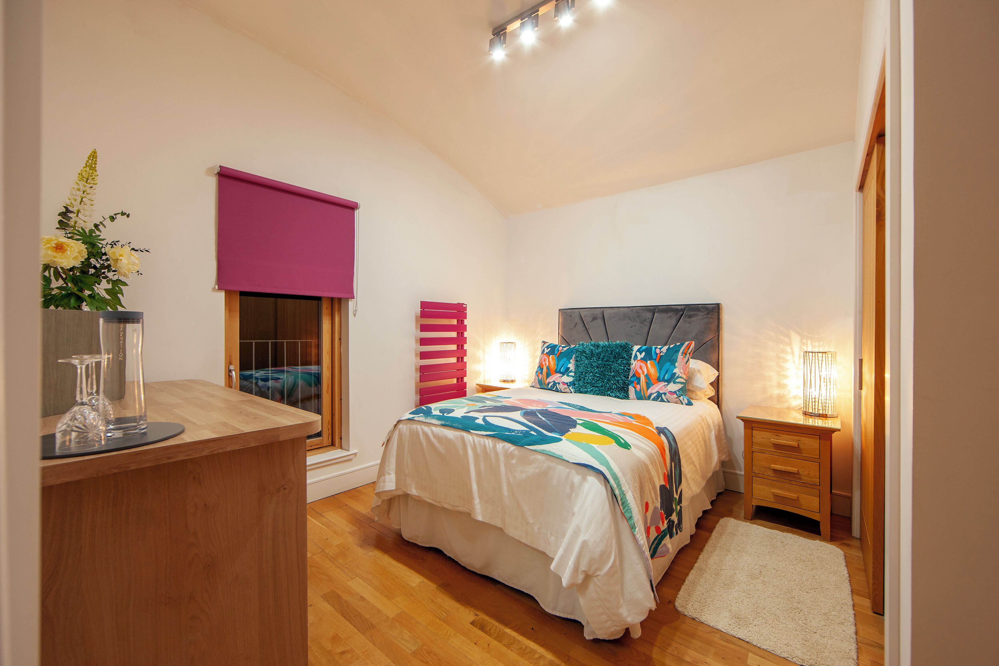 Un dormitorio con cama, mesitas de noche, un escritorio y una ventana con cortina.