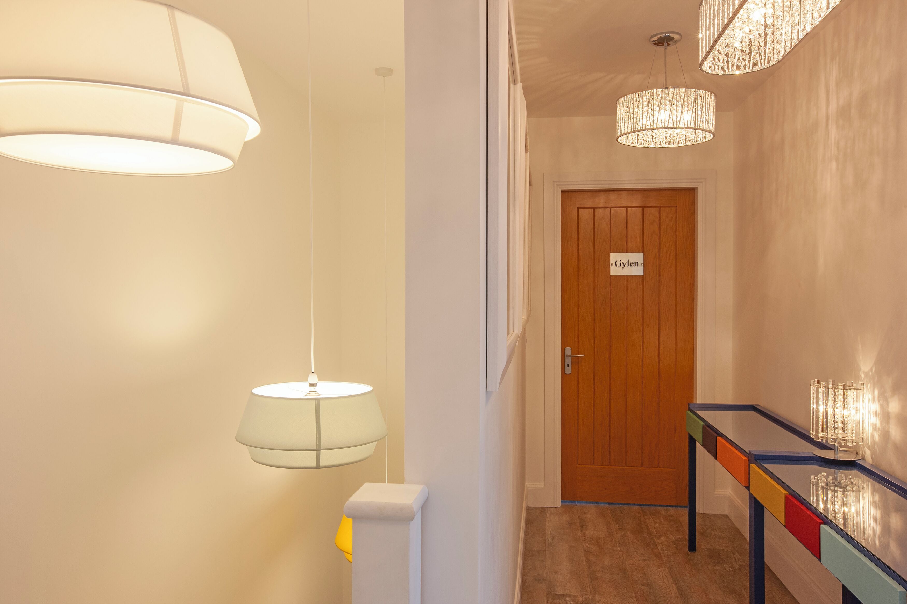 A hallway with a wooden door labeled "Gylens," a white radiator, and a table with colorful drawers.