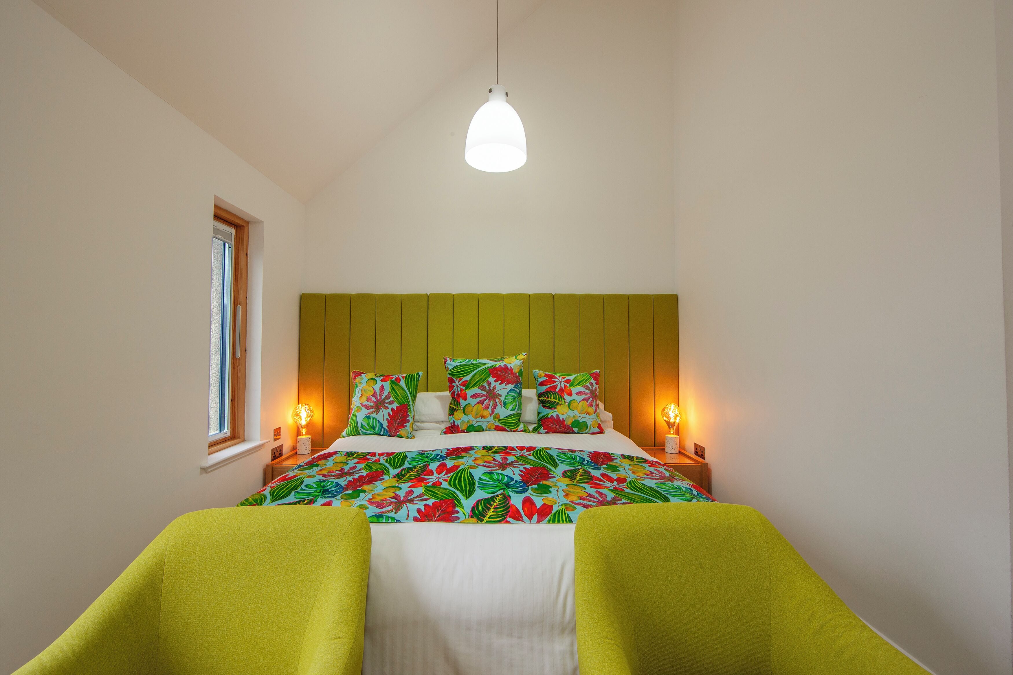 Un dormitorio con cama, dos mesitas de noche, una ventana y una lámpara colgante.