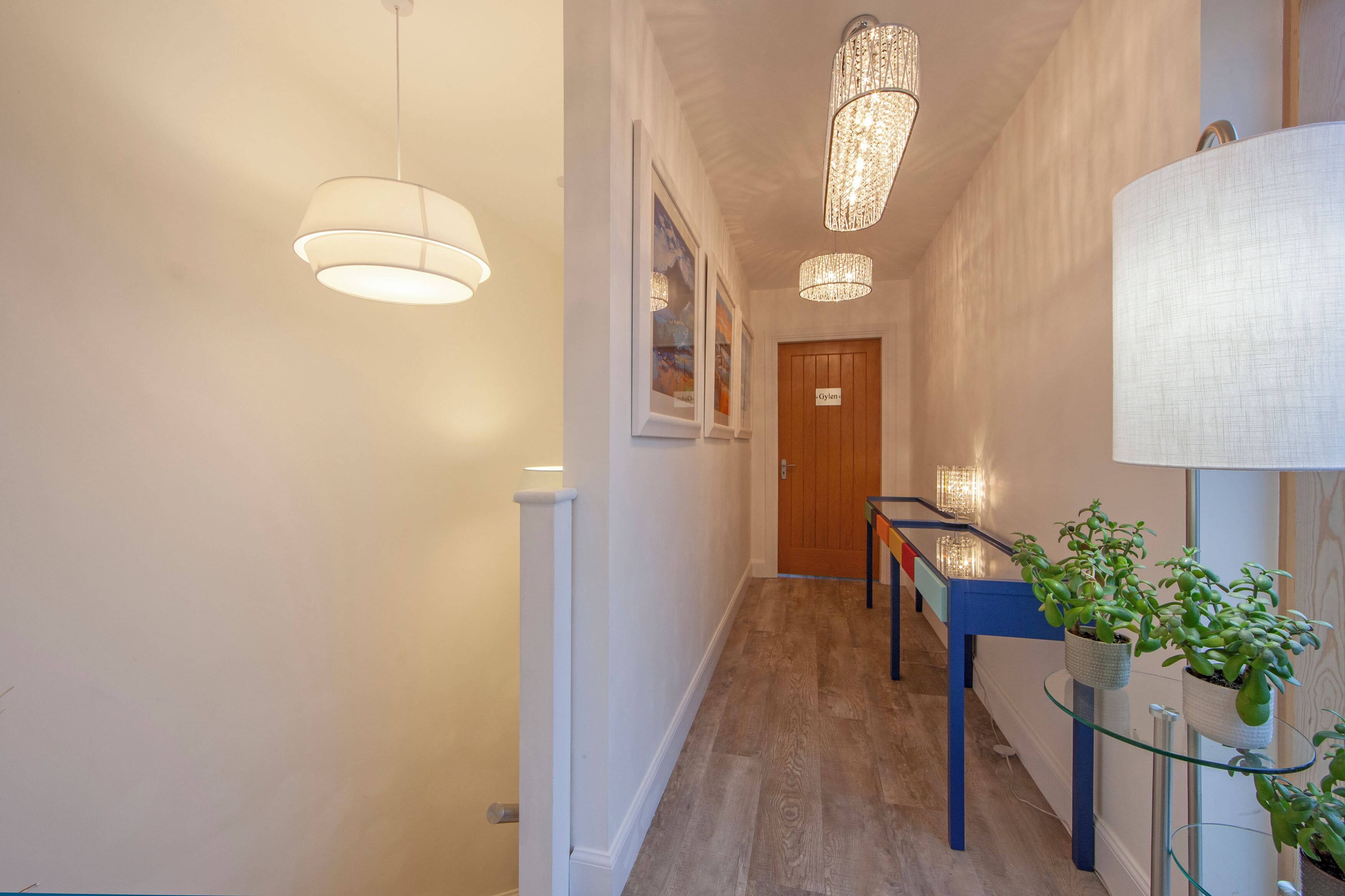 Un pasillo con suelo de madera, una mesa azul y una estantería de vidrio con plantas.