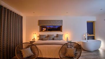 A bedroom with a large bed, two wicker chairs, a built-in bathtub, and a large window with a view.