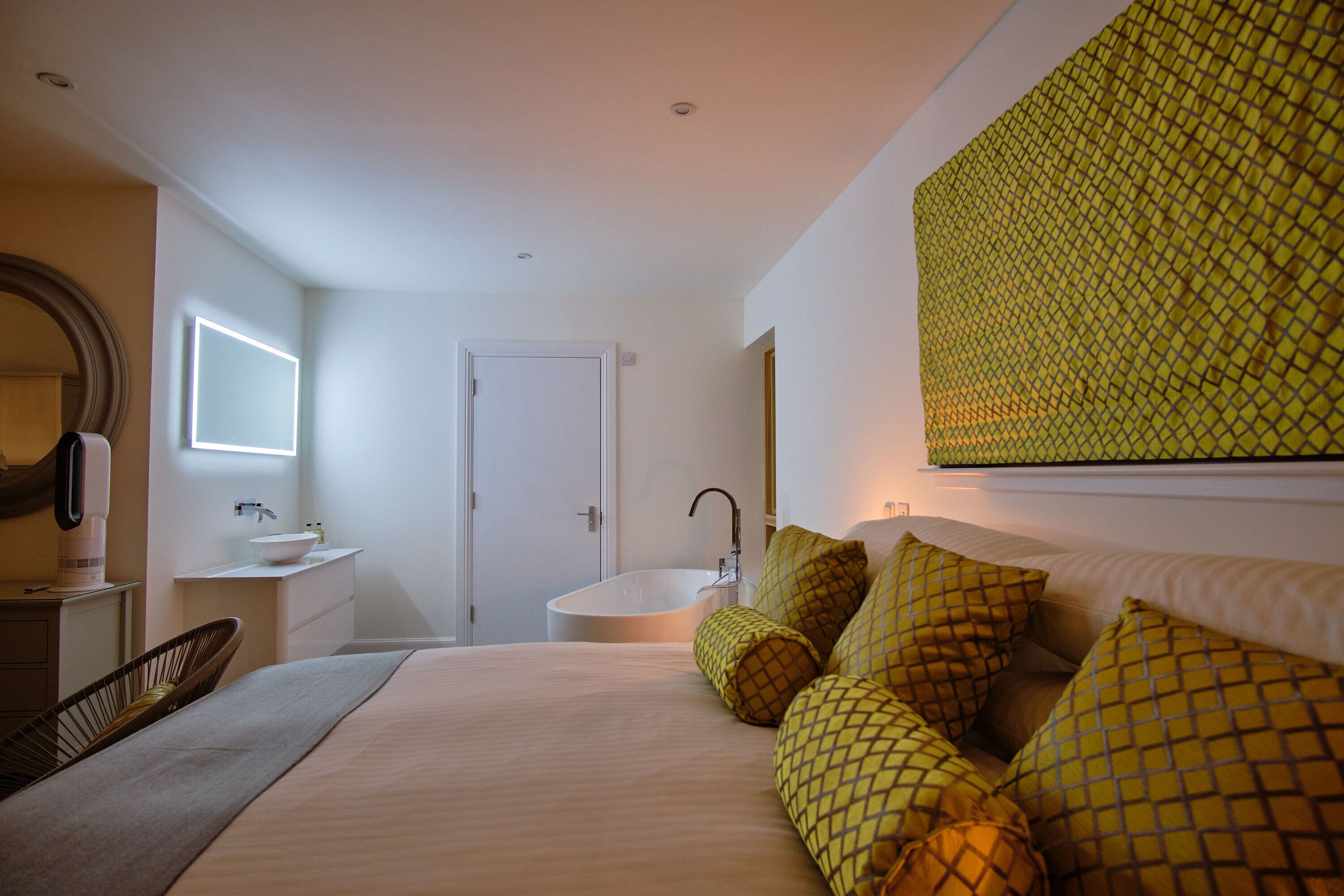 Un dormitorio con cama, mesita de noche, espejo, ventana y baño con lavamanos y bañera.