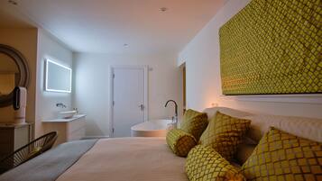 Un dormitorio con cama, mesita de noche, espejo, ventana y baño con lavamanos y bañera.