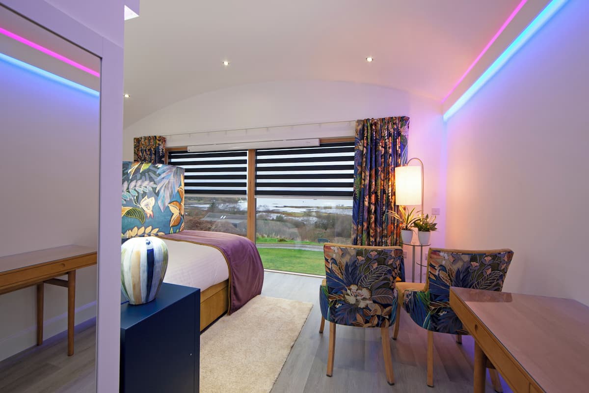A modern hotel room with a large bed, a desk, a chair, and a view of the outdoors.
