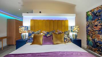 A hotel room with a large bed, a wooden headboard, two bedside tables with lamps, and a floral-patterned wall.