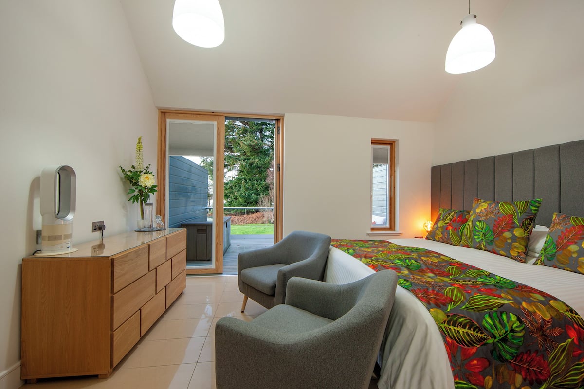 A bedroom with a bed, two chairs, a dresser, and a large window.