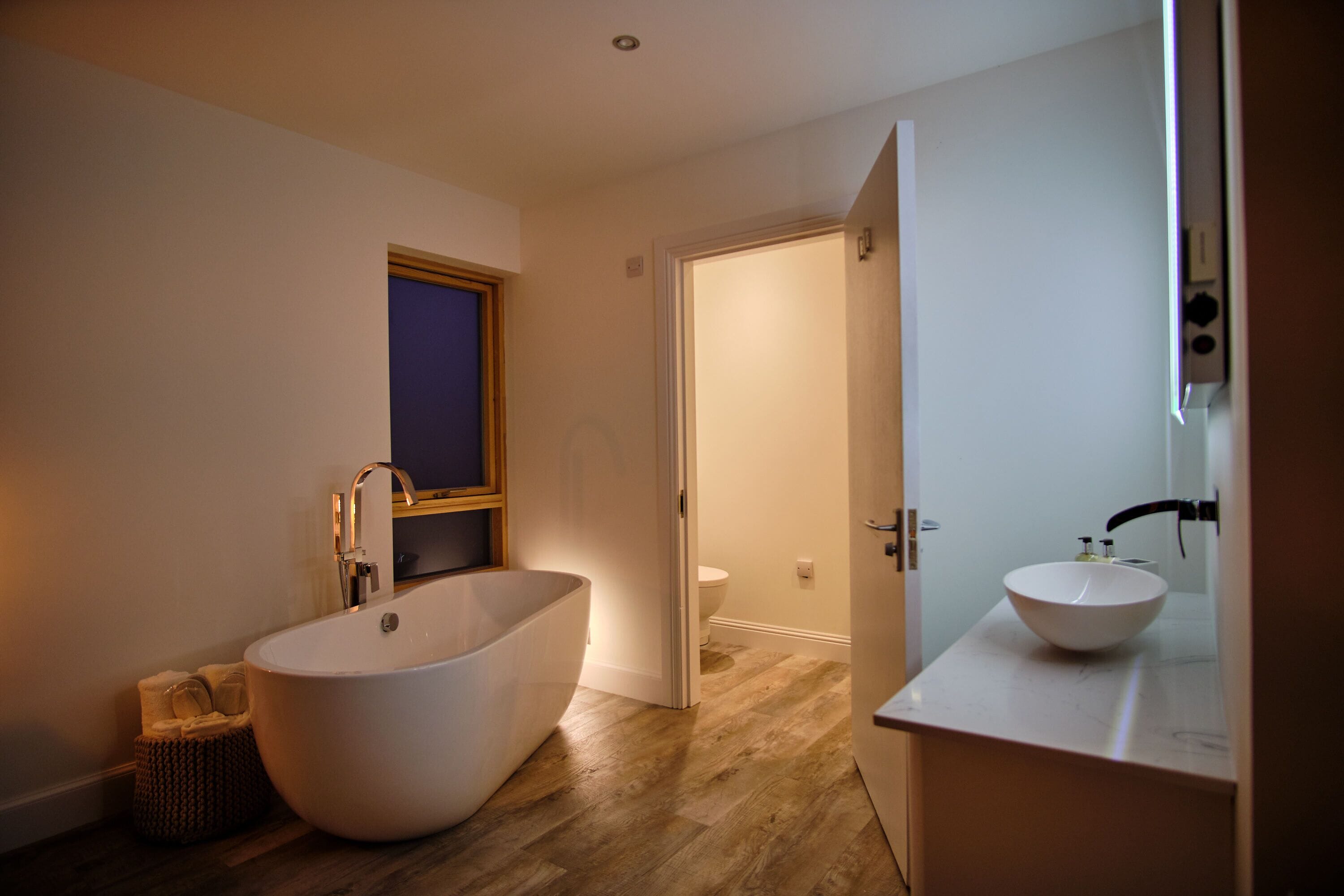 A modern bathroom with a freestanding bathtub, a sink with a mirror, and a wooden floor.