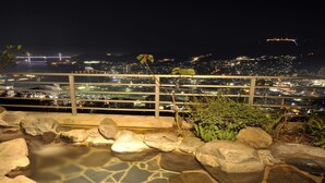 Une vue nocturne depuis un balcon doté d’une balustrade, donnant sur un paysage urbain avec des bâtiments illuminés et un pont.