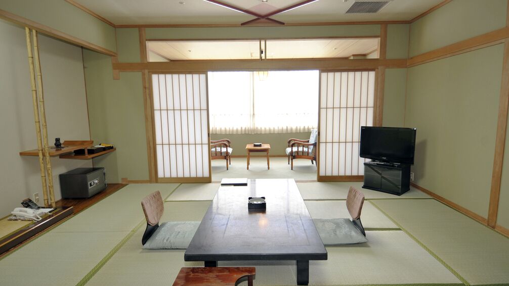 Une pièce de style japonais traditionnel, avec un sol recouvert de tatamis, une table basse avec des coussins, un téléviseur et des portes coulissantes.