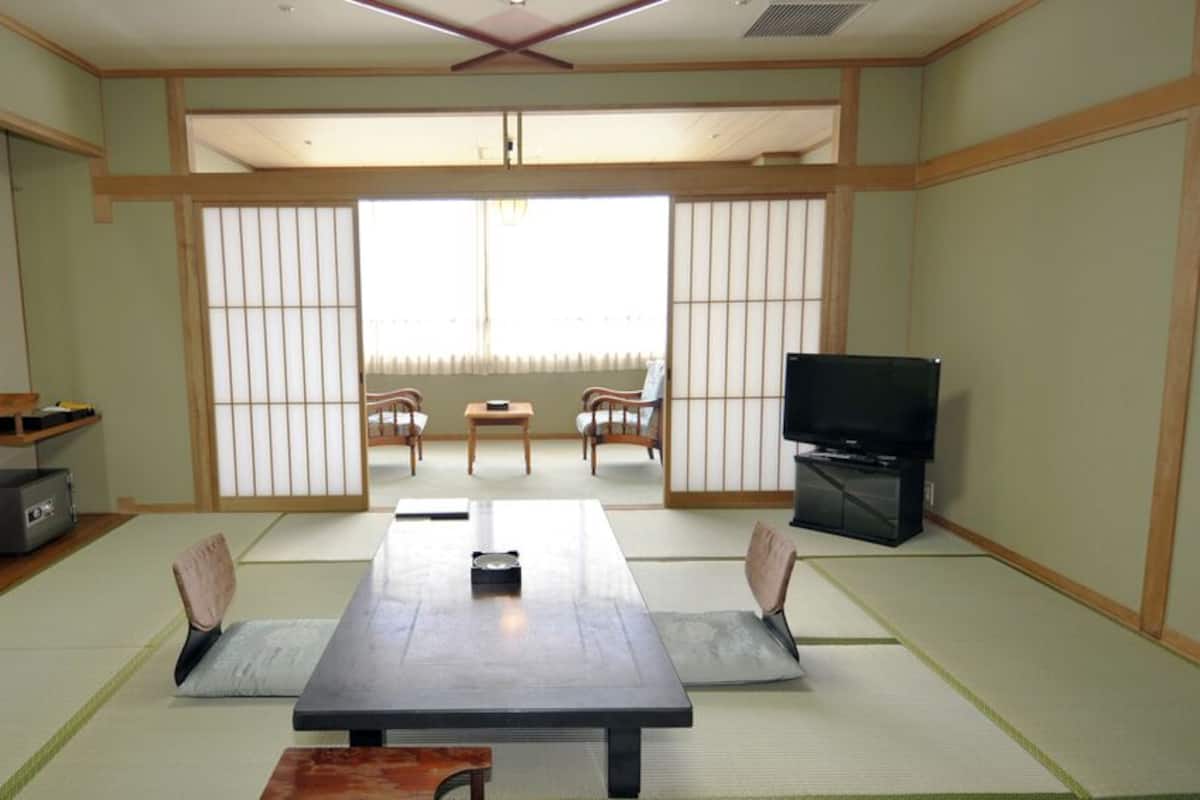Ein traditioneller japanischer Raum mit Tatami-Böden, einem niedrigen Tisch mit Kissen, einem Fernseher und Schiebetüren.