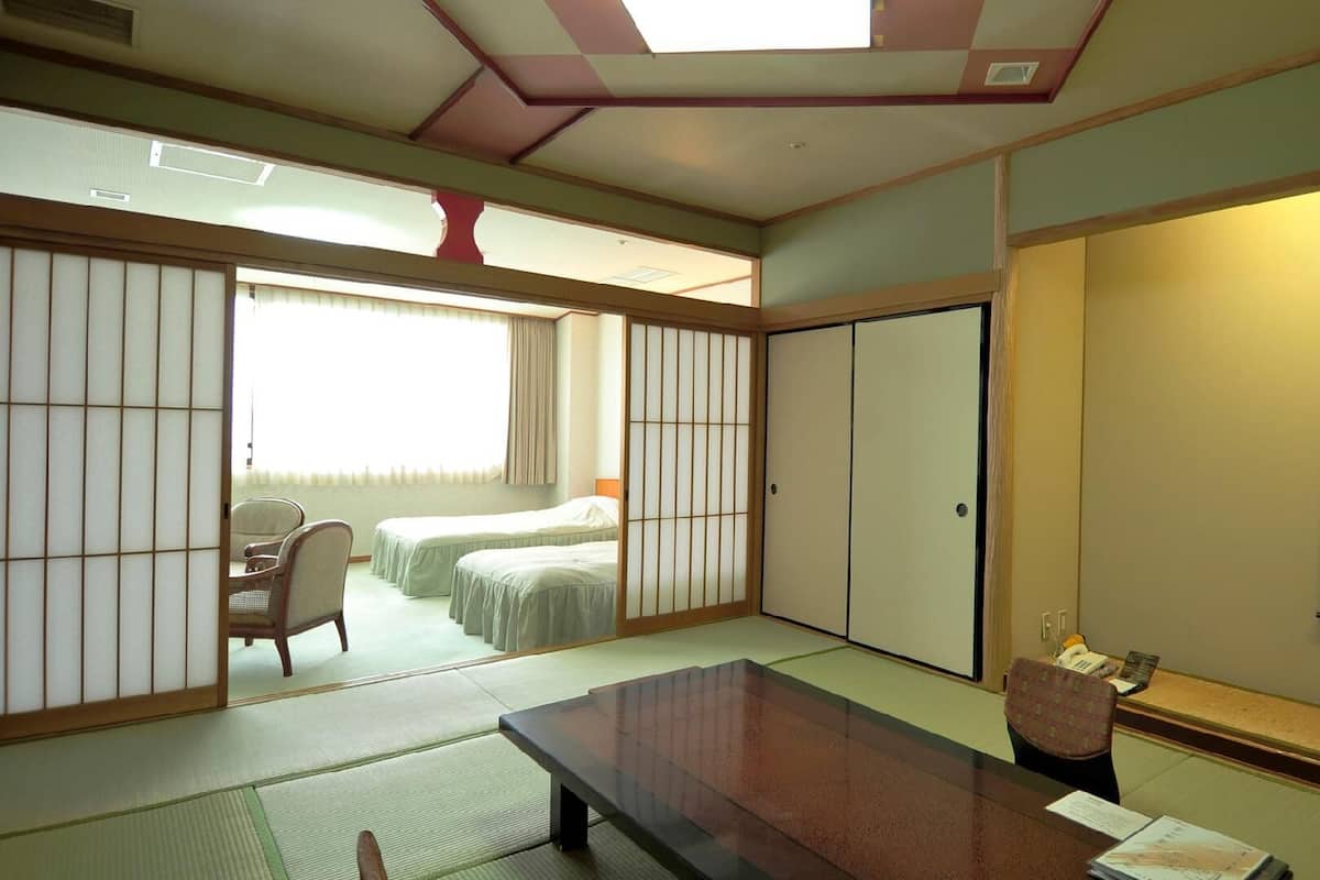Ein traditioneller japanischer Raum mit Tatami-Boden, einem niedrigen Tisch und einer verschiebbaren Tür zu einem Schlafzimmer.