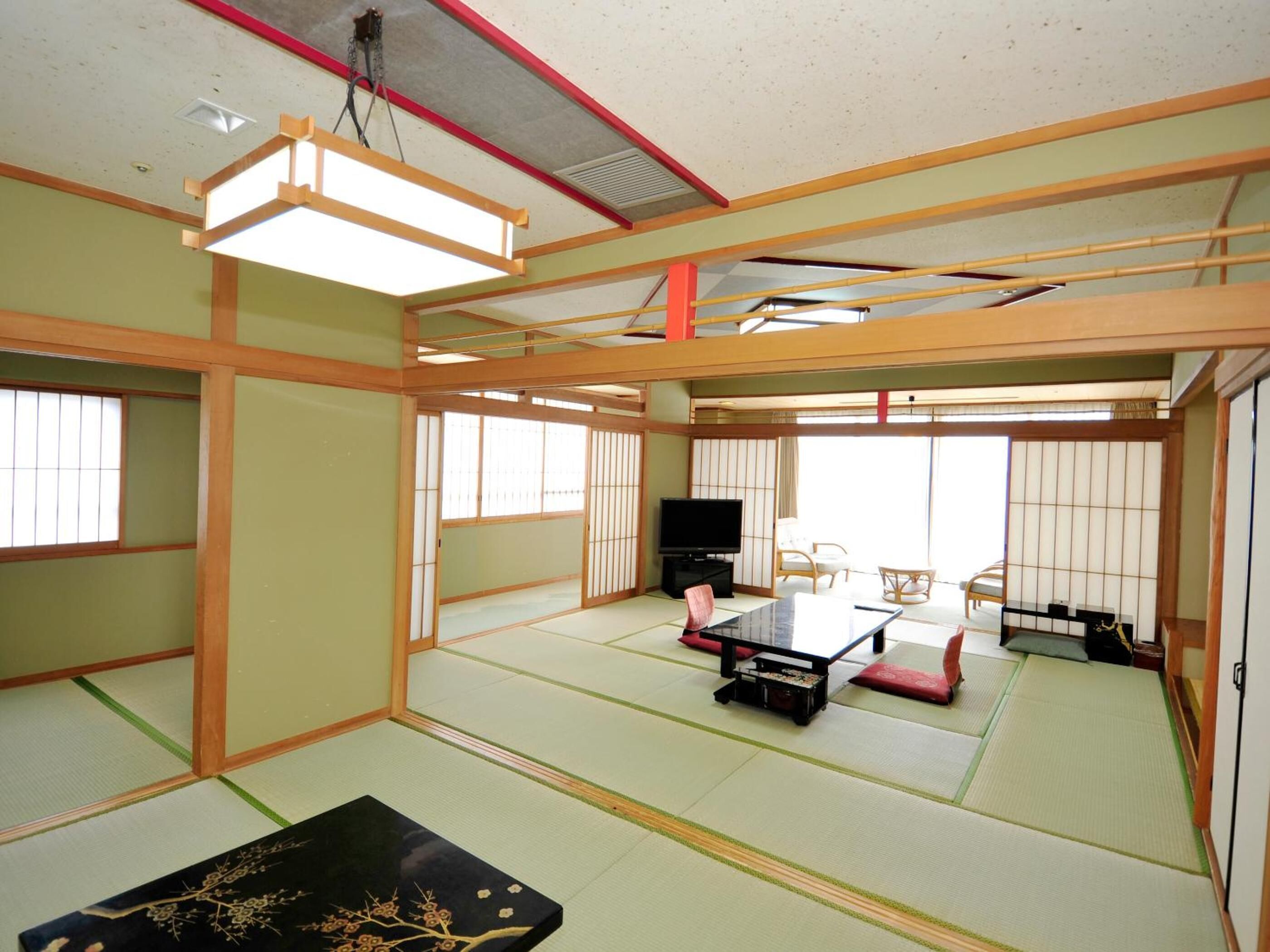 Ein Raum mit Tatami-Matten, einem Fernseher, einem kleinen Tisch und einem Futon.