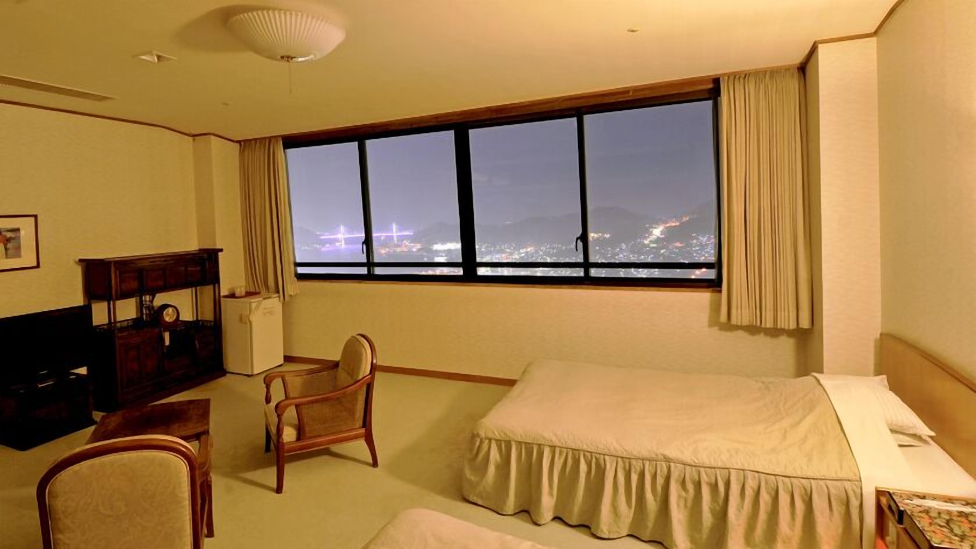 A hotel room with a large window, a bed, a chair, a desk, and a dresser.