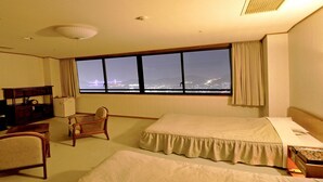 Une chambre d’hôtel avec une grande fenêtre, un lit, une chaise, un bureau et un téléviseur.