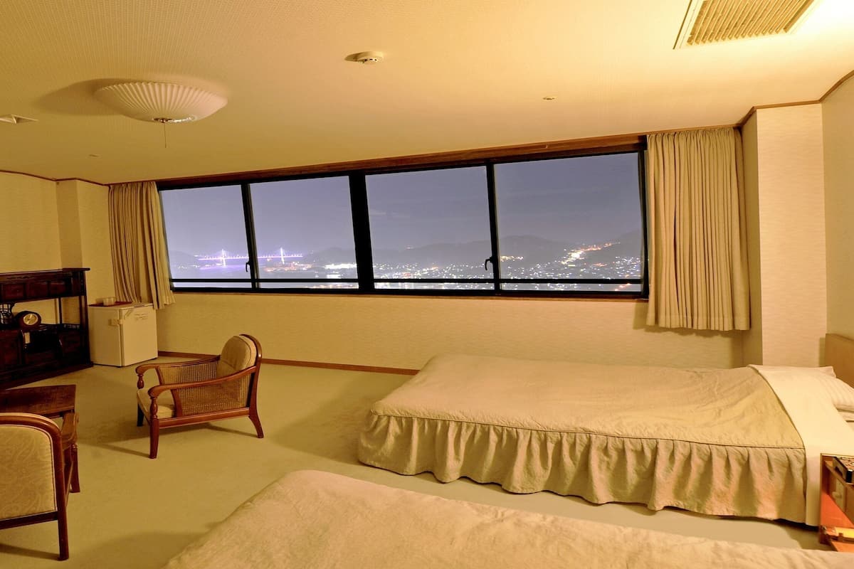 Ein Hotelzimmer mit großem Fenster, einem Bett, einem Sessel, einem Schreibtisch und einem Fernseher.