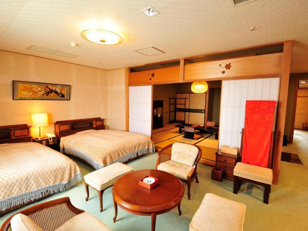 Habitación de hotel con dos camas, una zona de estar con mesa y sillas, una cortina roja y una puerta corrediza tradicional japonesa.