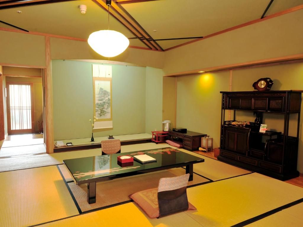 Une pièce de style japonais traditionnel, avec un sol recouvert de tatamis, une table basse, un meuble et un luminaire suspendu.