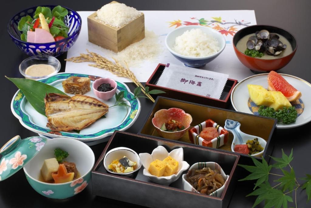 Ett urval av japanska rätter, inklusive ris, fisk och grönsaker, presenterade på ett bord med en bordsduk eller underlägg.