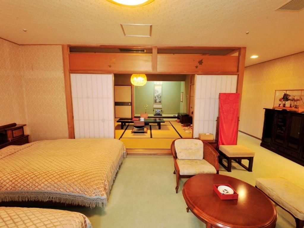 Une chambre d’hôtel avec un lit, une petite table, une chaise et un canapé. On peut apercevoir un coin repas à travers une porte coulissante.
