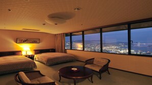 Une chambre d’hôtel avec deux lits, une chaise, une table et une grande fenêtre donnant sur la ville, avec une vue particulièrement agréable la nuit.