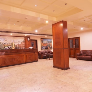 A lobby with a reception desk, leather sofas, a large wooden pillar, and a cityscape mural on the wall.