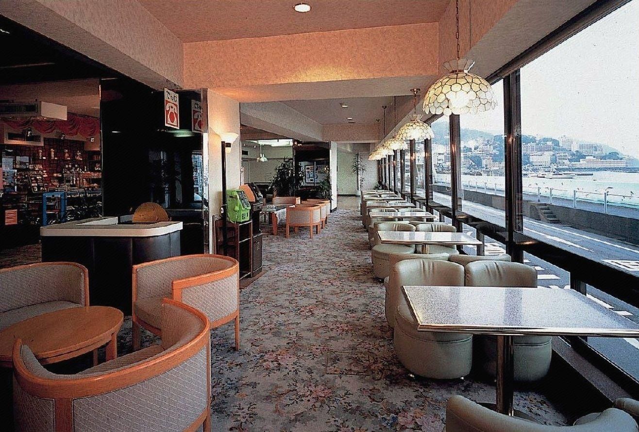 A restaurant with a long counter, multiple seating areas, and large windows overlooking a cityscape.