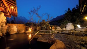 A stone hot spring area with a wooden fence, rocks, and a metal railing. - Yufunogo Saigakukan (Yufu)