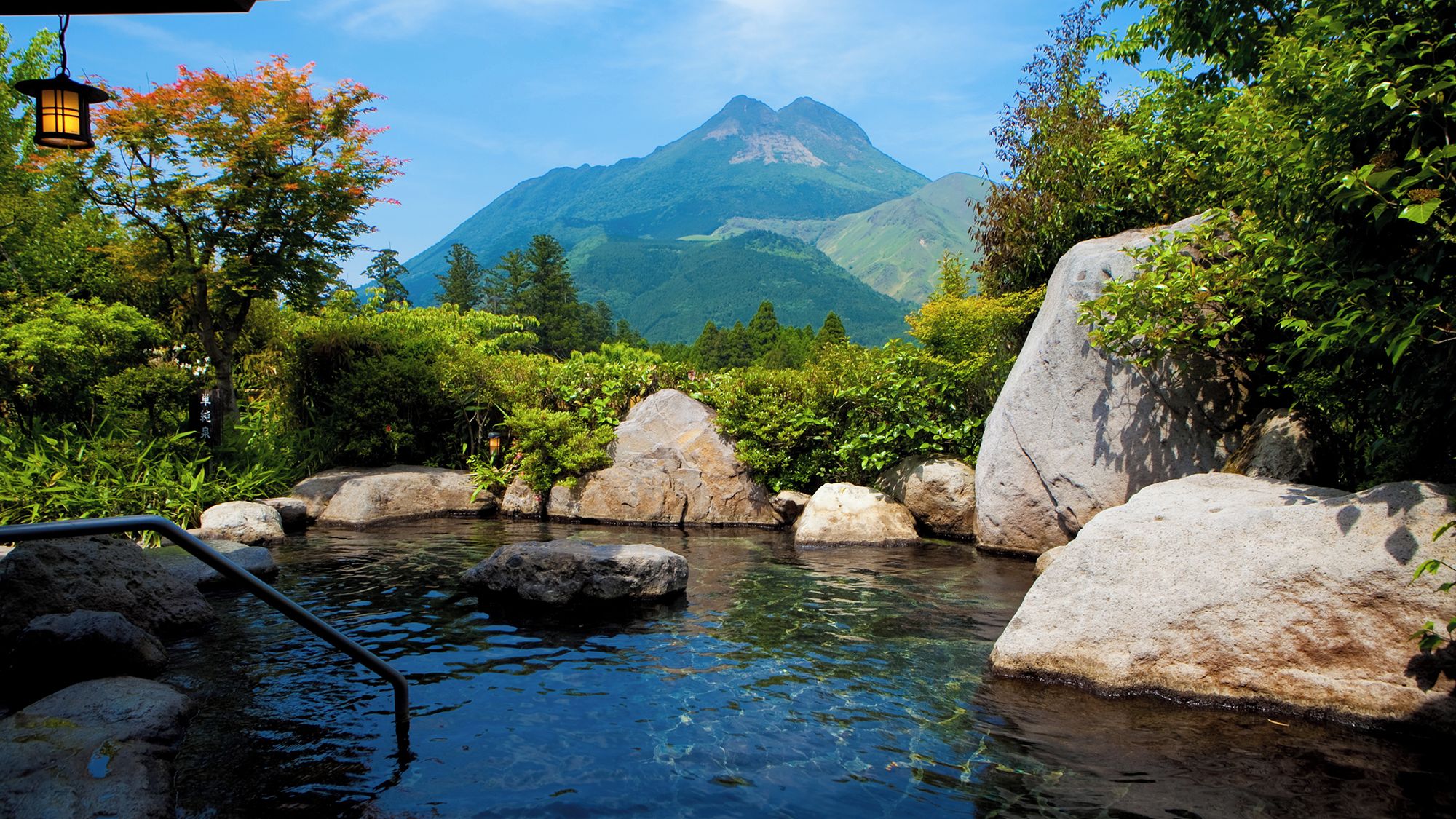 A tranquil outdoor setting with a clear stream, large rocks, and lush greenery.