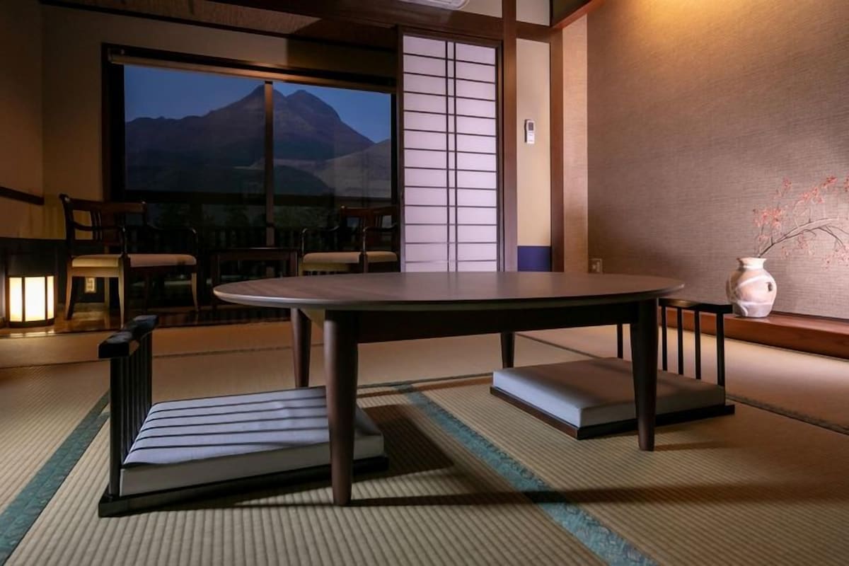 A traditional Japanese room with tatami flooring, a low table, and a view of a mountain.